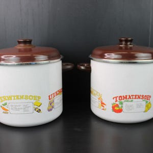 Pode incluir: Duas panelas de esmalte branco com tampas e alças marrons. Uma panela tem o texto "ERWTENSOEP" e a outra "TOMATENSOEP". Ambas as panelas apresentam ilustrações de vegetais e outros ingredientes.