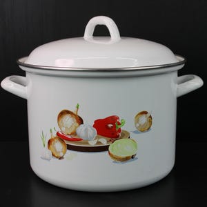 May include: White enamel cooking pot with lid and side handles. The pot features a colorful illustration of vegetables, including onions, a red pepper, and garlic. The pot has a silver rim and a loop handle on the lid.