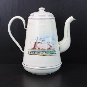 May include: White enamel coffee pot with a lid, handle, and spout. The pot features a painted scene of windmills, water, and birds. Gold trim accents the top and bottom. The pot is on a black surface.