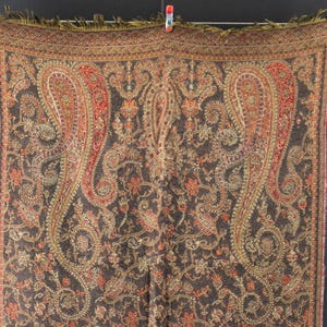 Peut inclure: Un châle marron avec un motif cachemire complexe dans des tons de rouge, orange et or. Le châle rectangulaire a une bordure à franges. Le motif présente de grands motifs cachemire incurvés et des éléments floraux.