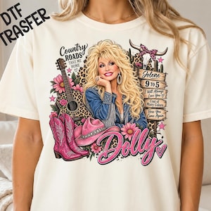 Peut inclure: Un t-shirt crème avec une impression graphique représentant une femme blonde, une guitare, des bottes de cow-boy roses, un chapeau rose et un crâne de vache. Le texte inclut "Country Roads", "Jolene", "9 to 5", "I Will Always Love You", "Coat of Many Colors" et "Dolly".