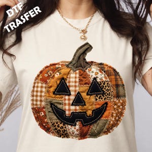 May include: A cream-coloured t-shirt featuring a large, central graphic of a patchwork pumpkin. The pumpkin is composed of various fabric patterns including plaid, floral, and leopard print, with black stitched eyes, nose, and mouth. Text reads DTF TRASFER.