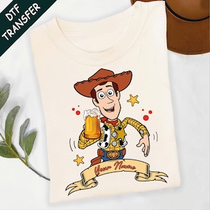Może przedstawiać: Kremowy t-shirt z rysunkowym kowbojem w brązowym kapeluszu, ż&oacute;łtej koszuli w kratę i kamizelce w łaty. Postać trzyma kufel piwa, otoczona ż&oacute;łtymi gwiazdkami i czerwonymi kropkami, z banerem poniżej z napisem Your Name na dole grafiki.