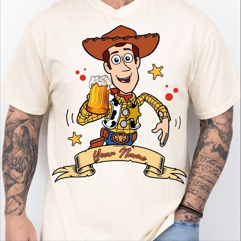 Może przedstawiać: Kremowy t-shirt z rysunkowym kowbojem w brązowym kapeluszu, ż&oacute;łtej koszuli w kratę i kamizelce w łaty. Postać trzyma kufel piwa nad beżowym banerem z czerwonym napisem Your Name.