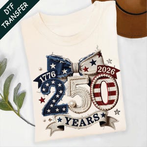 May include: Cream-colored t-shirt with a patriotic design featuring a bow, the numbers "250", and the years "1776" and "2026". The design incorporates red, white, and blue colors, stars, and pearl accents. The words "YEARS" are displayed on a banner.
