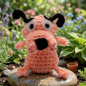 May include: A peach-colored crochet dog plushie with large white eyes, black felt pupils, and floppy black ears. The handmade toy features a prominent black nose and a textured yarn body, standing in a simple, upright, and wide-eyed expression.