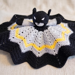 Puede incluir: Una manta de seguridad de ganchillo hecha a mano con un personaje de Batman. La manta es negra, gris y amarilla, con forma de estrella. La figura de Batman tiene una cabeza negra con detalles blancos y orejas pequeñas. Para bebés y niños pequeños.
