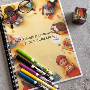 Peut inclure: Un cahier d'apprentissage spiralé avec le titre "MON CAHIER D'APPRENTISSAGE ET DE VALORISATION" et le texte "50 PAGES". L'image montre également une paire de lunettes, des marqueurs colorés et un petit cube jouet.