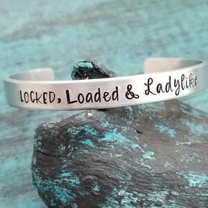 Op de afbeelding: Zilveren armband met de inscriptie "LOCKED, Loaded & Ladylike".