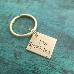 Pu&ograve; includere: Un portachiavi dorato con un'etichetta quadrata che recita "I'm Speaking".