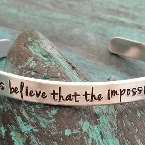 Op de afbeelding: Zilveren armband met de inscriptie "Geloof altijd dat het onmogelijke mogelijk is".