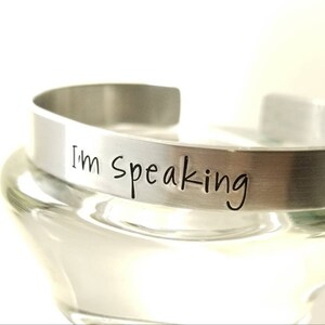 Pu&ograve; includere: Un braccialetto in metallo argentato con le parole "I'm Speaking" incise.