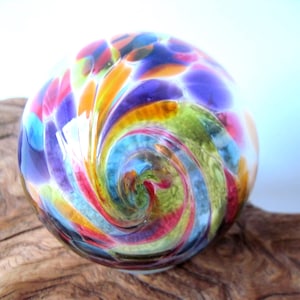 May include: A spherical glass paperweight featuring a swirling, multi-colored pattern of purple, lime green, orange, red, and blue hues. The surface is smooth and reflective, showcasing a vibrant, blended design that radiates from the center outward.