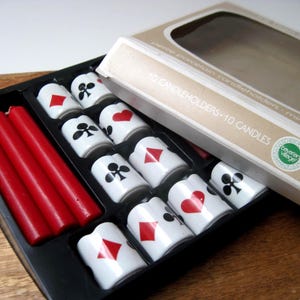 Può includere: Un vassoio nero contiene portacandele in porcellana bianca decorati con simboli di carte da gioco e candele rosse. La scatola recita "10 CANDLEHOLDERS - 10 CANDLES". I portacandele sono progettati per le candele rosse.