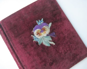 May include: A burgundy velvet photo album with an embroidered pansy flower in shades of purple, white, and blue.