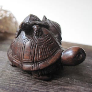 May include: A dark brown wooden sculpture of two turtles, one on top of the other. The sculpture is carved with intricate details and has a smooth, polished finish.