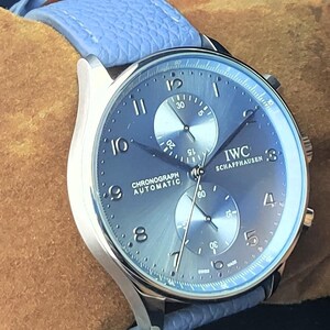 Puede incluir: Un reloj cron&oacute;grafo IWC Schaffhausen plateado con esfera azul y correa de cuero azul claro. La esfera del reloj muestra el texto "CHRONOGRAPH AUTOMATIC" y tiene dos subesferas. El reloj est&aacute; sobre un fondo marr&oacute;n.