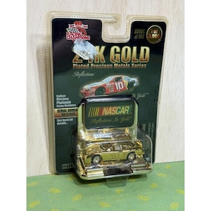 May include: A gold-plated NASCAR die-cast car in a clear plastic case. The packaging reads "24K GOLD Plated Precious Metals Series" and "Reflections In Gold." The car is a collectible item from Racing Champions.