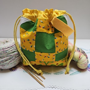 May include: A drawstring pouch featuring a patchwork design of yellow fabric with small colorful ice cream cone prints and solid green squares. The bag has a yellow drawstring closure, a yellow woven handle, and a yellow fabric interior lining.