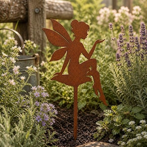 May include: A rust-colored metal garden stake featuring a silhouette of a fairy with wings, sitting on a mushroom shape. The figure has a bun hairstyle and one arm extended outward. The metal has a textured, weathered brown finish throughout.
