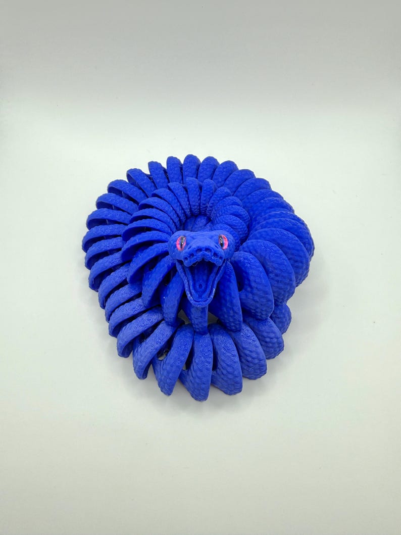 Pode incluir: Escultura de cobra azul enrolada, com um corpo texturizado e detalhado. A cabe&ccedil;a da cobra est&aacute; levantada, revelando uma boca bem aberta e olhos rosa. A escultura est&aacute; sobre um fundo branco liso.