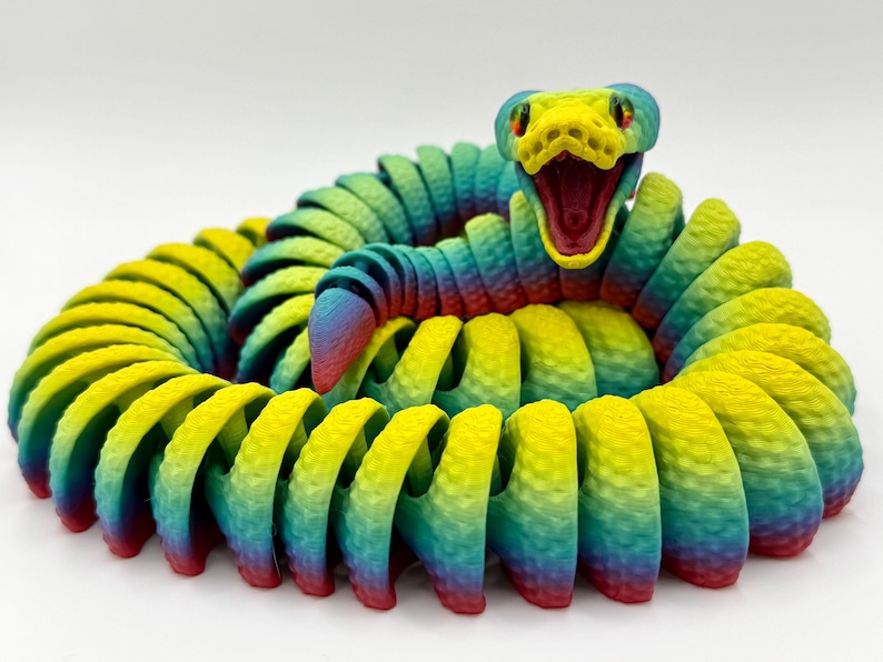 Pode incluir: Um brinquedo de cobra colorido e articulado em posi&ccedil;&atilde;o enrolada. A cobra apresenta um gradiente de cores, incluindo amarelo, verde, azul e vermelho. A cabe&ccedil;a da cobra est&aacute; aberta, revelando um interior vermelho. O brinquedo tem uma superf&iacute;cie texturizada.