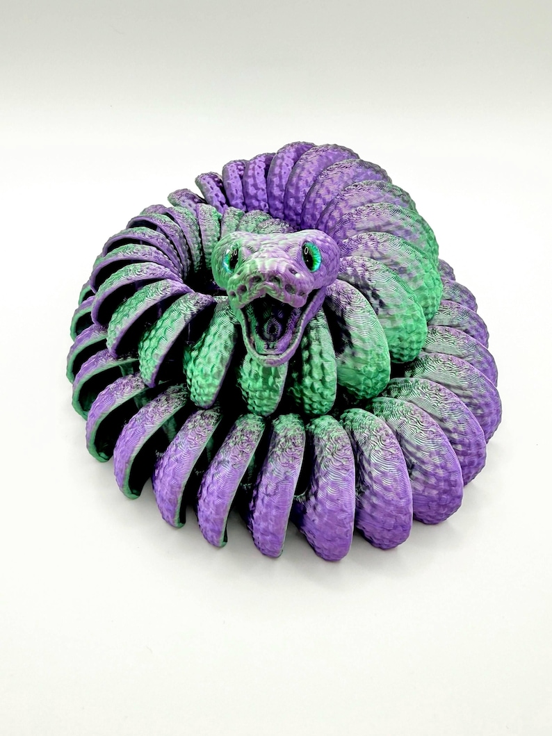 Pode incluir: Um brinquedo de cobra impresso em 3D em tons de roxo e verde. A cobra est&aacute; enrolada, com a cabe&ccedil;a levantada e a boca aberta. Os olhos s&atilde;o verdes. O brinquedo tem uma superf&iacute;cie texturizada e est&aacute; sobre um fundo branco.