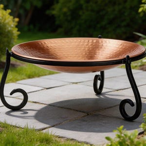 May include: A copper fire pit with a hammered texture bowl and a black metal frame. The fire pit has a circular design and is supported by three curved legs. The fire pit is designed for outdoor use.