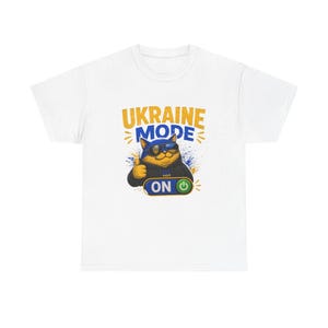 May include: White t-shirt featuring a cartoon cat wearing sunglasses and a jacket, with the text "UKRAINE MODE ON" in yellow and blue. The cat is giving a thumbs up, with blue and yellow accents.
