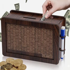 May include: A rectangular dark brown wooden money box featuring a grid of numbers on the front panel, a coin slot on top, and a white marker with a blue cap attached to the side. The front panel displays various dollar amounts and a 10.000 $ label.