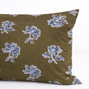 Può includere: Cuscino verde oliva con un motivo floreale ripetuto. I fiori sono blu e bianchi, con dettagli intricati di petali e foglie. Il cuscino ha un aspetto morbido e strutturato, che suggerisce un comodo elemento di arredo per la casa.