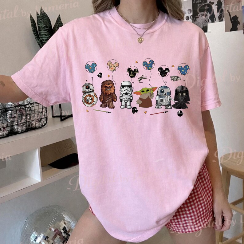 Puede incluir: Camiseta rosa claro con una ilustraci&oacute;n de personajes de Star Wars y globos tem&aacute;ticos de Mickey Mouse. Los personajes incluyen BB-8, Chewbacca, un Stormtrooper, Grogu, R2-D2 y Darth Vader. Los globos son azules, amarillos y negros.