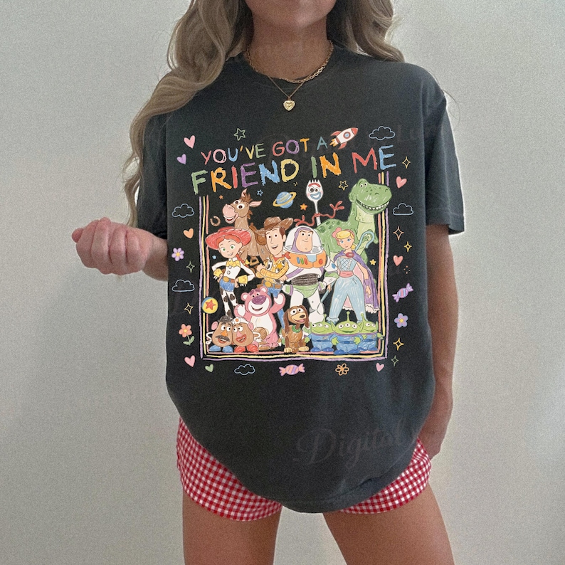 May include: Dark gray t-shirt featuring a colorful graphic of Toy Story characters with the text "YOU'VE GOT A FRIEND IN ME". The design includes Woody, Buzz Lightyear, and other characters from the movie.