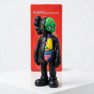 May include: A black KAWS Companion figure with a partially dissected body revealing internal organs. The figure has a green brain, a yellow and blue torso, and a red box in the background with the text "KAWS COMPANION".