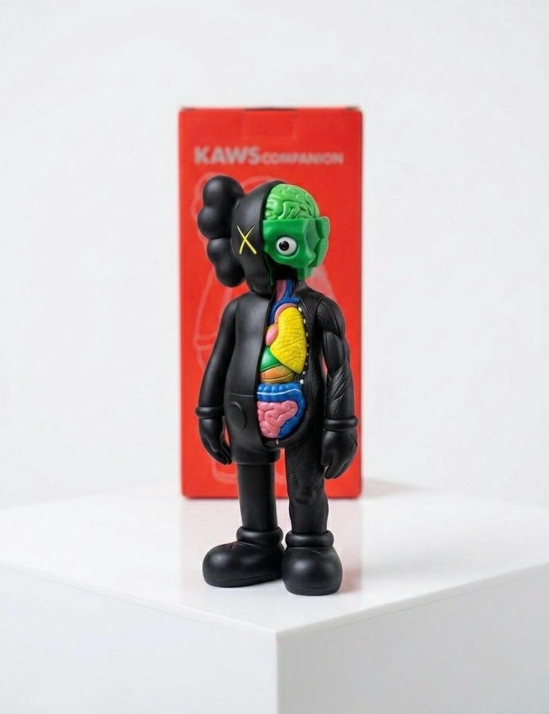 May include: A black KAWS Companion figure with a partially dissected body revealing internal organs. The figure has a green brain, a yellow and blue torso, and a red box in the background with the text "KAWS COMPANION".