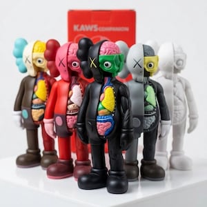 May include: A collection of KAWS Companion figures in various colors, each with a unique anatomical design. The figures are arranged in a row, showcasing their distinct color schemes and internal organ details. A red box with the text "KAWS COMPANION" is in the background.