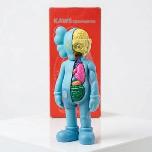 May include: A blue KAWS Companion figure with exposed internal organs, including a pink heart and green intestines. The figure has a partially dissected head revealing a yellow brain. The figure stands in front of a red box with the text "KAWS COMPANION".