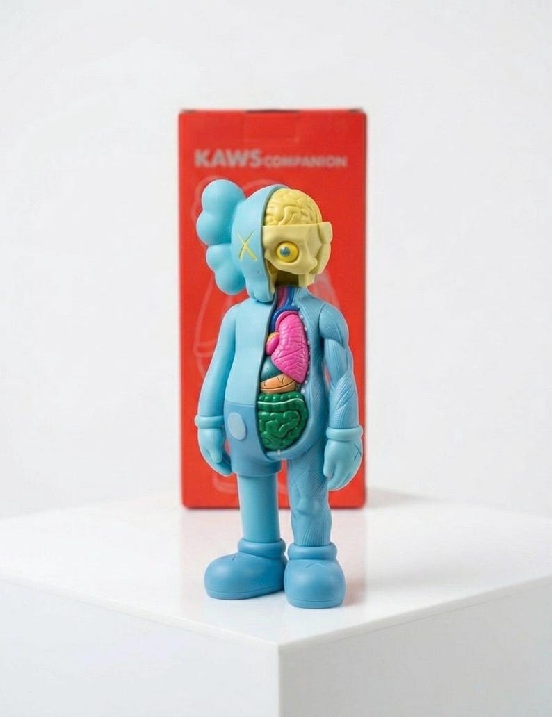 May include: A blue KAWS Companion figure with exposed internal organs, including a pink heart and green intestines. The figure has a partially dissected head revealing a yellow brain. The figure stands in front of a red box with the text "KAWS COMPANION".