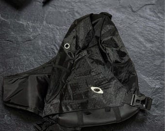 Puede incluir: Una mochila bandolera negra con un sutil patrón hexagonal, un bolsillo lateral de malla, un ojal metálico plateado y un cierre de hebilla de plástico negro. Un pequeño logotipo bordado en blanco está centrado en el panel frontal.