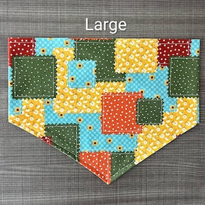 May include: A triangular pet bandana featuring a patchwork pattern of squares in red, dark green, yellow, and light blue. The fabric displays a repeating sunflower print across the colored sections. The word Large is printed in white text above.