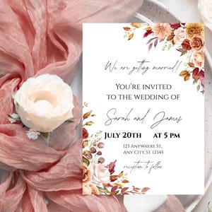Könnte beinhalten: Eine Hochzeitseinladung mit floralen Akzenten und dem Text "We are getting married!". Die Einladung enthält die Namen Sarah und James, das Datum 20. Juli um 17:00 Uhr und eine Adresse. Die Einladung ist von rosa Stoff und einer weißen Blume umgeben.