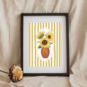 Könnte beinhalten: Gerahmter Kunstdruck mit einer Aquarellillustration von Sonnenblumen in einer Terrakotta-Vase. Die Sonnenblumen sind vor einem gelb-weiß gestreiften Hintergrund platziert und in einem schwarzen Rahmen eingefasst. Das Kunstwerk hat eine warme, sommerliche Ausstrahlung.