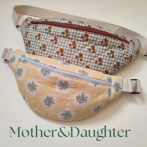Puede incluir: Dos riñoneras acolchadas con correas ajustables. La bolsa superior presenta un patrón de cuadros vichy en verde salvia y blanco con pequeñas flores naranjas y una cremallera color óxido. La bolsa inferior es amarilla con estampado floral azul y cremallera azul claro.
