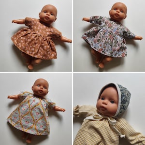 Könnte beinhalten: Vier Babypuppen mit verschiedenen Kleidern und Mützen. Die Kleider weisen verschiedene Blumen- und Musterdesigns in Braun-, Blau- und Gelbtönen auf. Die Puppen sind vor einem weißen Hintergrund positioniert.