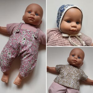 Könnte beinhalten: Eine Babypuppe mit blauen Augen in verschiedenen Outfits, darunter eine rosa geblümte Latzhose über einem rosa Shirt, eine blaue geblümte Haube mit braunem Karohemd und ein grünes geblümtes Oberteil mit rosa Hose. Die Puppe hat einen hellen Teint.