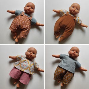 Könnte beinhalten: Vier Babypuppen in verschiedenen Outfits. Eine Puppe trägt ein blaues Hemd und eine braune Blumen-Latzhose. Eine andere Puppe trägt eine braune Cord-Latzhose. Die dritte Puppe trägt ein geblümtes Oberteil und rosa Shorts. Die letzte Puppe trägt ein blaues Hemd und eine braune Blumenhose.