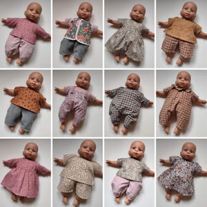 Könnte beinhalten: Eine Sammlung von Babypuppen in verschiedenen Outfits. Die Puppen tragen verschiedenfarbige Oberteile und Hosen, darunter geblümte Kleider, gemusterte Hemden und karierte Overalls. Die Outfits sind in Rosa-, Braun- und Grüntönen gehalten.