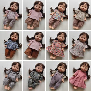 Könnte beinhalten: Eine Sammlung von Puppen, jede mit braunen Zöpfen, die verschiedene Outfits tragen. Die Outfits umfassen Blumenmuster, unifarbene Kleidung und Latzhosen. Die Puppen liegen, um die verschiedenen Kleidungsstile zu zeigen.