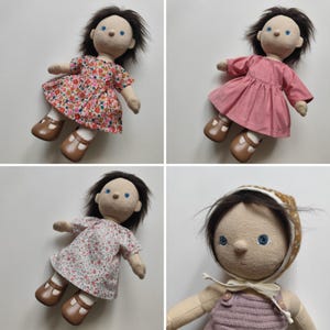 May include: Four handmade cloth dolls with brown hair and blue eyes. The dolls are dressed in various dresses, including floral and solid pink. Each doll has brown shoes. One doll wears a bonnet.