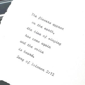 May include: A handwritten quote from Song of Solomon 2:12 on a torn piece of white paper. The text, in black ink, reads: "The flowers appear on the earth, the time of singing has come again and the voice is heard."